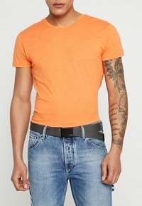 Kortærmet orange T-shirt lavet af bomuld, kombineret med lyseblå jeans i denim og et sort bælte med en rektangulær spænde.