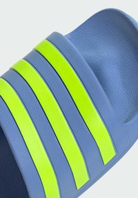 Plave klizne sandale s teksturiranom površinom, s tri debele neon žute pruge na gornjem dijelu. Glatki, zakrivljeni dizajn, stil s otvorenim prstima.