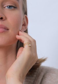 Set de inele din aur format din două benzi suprapuse: una texturată cu un model în zigzag, cealaltă cu un mic accent decorativ. Tonul pielii este vizibil.