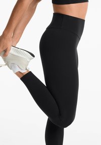 Fekete, magas derekú leggings sima, rugalmas textúrával, sportoláshoz tervezve. Szoros illeszkedésű sziluett és minimális varrások jellemzik.
