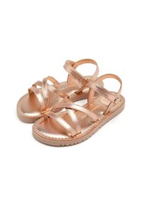 Sandalias en oro rosa con múltiples tiras cruzadas. Fabricadas en material sintético brillante, cuentan con una suela texturizada y un acabado suave.
