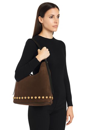 Bruine suède schoudertas met gouden ronde studs langs de onderkant, voorzien van een soepele zwarte lederen schouderband en een slouchy ontwerp.
