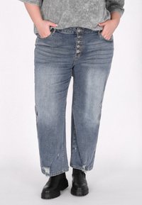 Jeans din denim albastru deschis, cu talie înaltă, închidere cu cinci nasturi, detalii distruse și picioare drepte, asortați cu cizme negre până la gleznă.