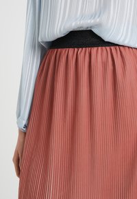 Plisseret nederdel i en blød, rosefarvet nuance med en tekstureret sort elastisk talje. Toppen har lyseblåt, gennemsigtigt stof med lodrette striber.