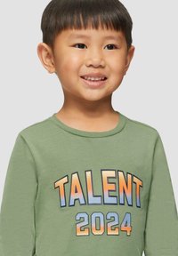 Langarmige grüne Baumwollbluse mit dem Schriftzug "TALENT 2024" in blauer und orangefarbener Farbverlauf-Schrift. Weicher Stoff mit klassischem Rundhalsausschnitt.