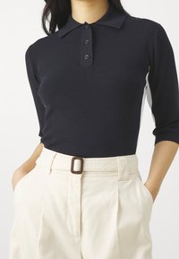 Zwarte, getailleerde longsleeve polo met kraag en een drievoudige knopenrij, gecombineerd met romig witte high-waisted broek met een riem.