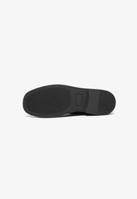 Semelle de chaussure noire avec un motif de grip texturé, section de talon rectangulaire et zone de cambrure lisse sur fond blanc.