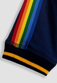 Pantalones cortos azul marino con rayas de arcoíris en rojo, naranja, amarillo, verde y azul a los lados, y un dobladillo a rayas amarillo.