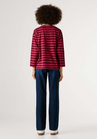 Majica dugih rukava s prugama u tamnoružičastoj i svijetloružičastoj boji, s okruglim izrezom, uparena s tamnoplavim trapericama ravnih nogavica i bijelim tenisicama.