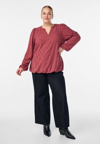 Röd mönstrad blus med långa ärmar och V-ringning, i kombination med mörka denimbyxor med vida ben och svarta ankelstövlar.