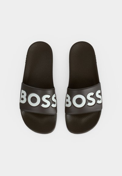 Paire de sandales slides noires avec semelles texturées et larges brides affichant le mot BOSS en grosses lettres blanches.