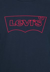 Levi's logotyp i röd kontur på mörkblått tyg, med registrerat varumärkessymbol i övre högra hörnet.