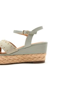 Sandal con tacco a cuneo verde chiaro, con fascia borchiata e fibbia alla caviglia, caratterizzata da una piattaforma in juta intrecciata e suola in gomma marrone.
