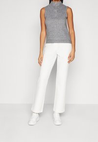 Grijze mouwloze top met een nepbodem en een rits aan de voorkant, gecombineerd met witte wijde broekspijpen en witte sneakers. Gladde textuur, casual pasvorm.