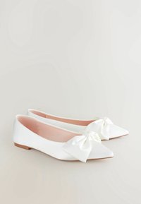 Ballerines blanches avec un bout pointu et un grand nœud en satin à l'avant. Tissu lisse et semelle intérieure rose avec un petit talon plat.
