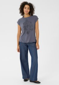 Grå kortærmet t-shirt med et sort dekorativt print, parret med brede mørk denimbukser og sorte flade sko. Enkel design og afslappet pasform.