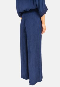 Pantalons évasés en tissu texturé bleu marine, avec une taille haute et un design fluide, adaptés pour un usage décontracté ou formel.