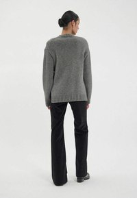 Pull en tricot gris avec ourlet côtelé, coupe décontractée et épaules tombantes, associé à un pantalon noir évasé. Le tissu a une texture douce.