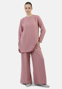 Losse, lange mouw top en wijde broek van zacht roze stof met een gestructureerde afwerking. Kenmerken zijn onder andere zijzakken en een ronde halslijn.