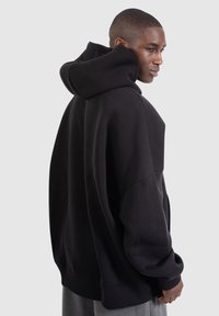 Black oversized hoodie with a hood, ribbed cuffs, and hem. Soft fabric, smooth texture. Displayed on a model seen from the side.