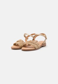 Flache Sandalen in einem hellbraunen Farbton, mit geflochtenen, strukturierten Riemen und einer verstellbaren Schnalle am Knöchel. Glatte Sohle und lässiges Design.
