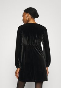 Robe en velours noir avec des manches longues, un col rond et une taille froncée. Texture lisse et coupe légèrement ample.