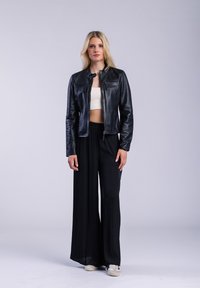 Černá kožená zkrácená bunda na zip, v kombinaci s černými kalhotami s širokým střihem a bílými teniskami. Hladký povrch a jednoduchý design.