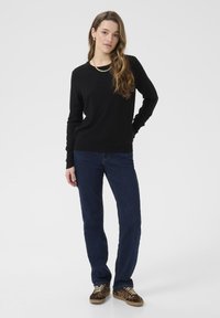 Maglione nero, jeans blu scuro e sneakers con stampa leopardata. Il maglione ha un collo a giro, polsini aderenti e una texture di tessuto liscia.