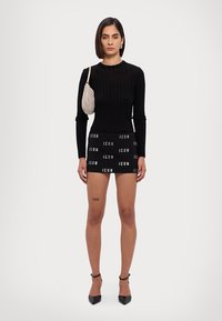 Zwarte geribbelde lange mouw top, zwarte mini rok met witte tekst "ICON", glanzende zilveren tas, zwarte hoge hakken, zichtbare tatoeage op het dijbeen.
