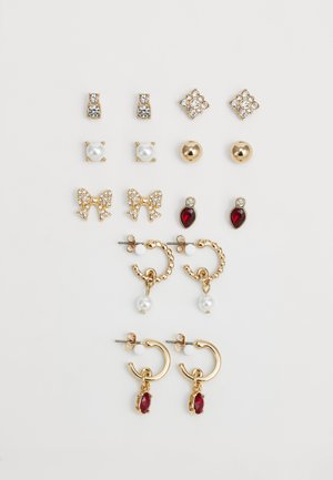 Ni par guld- og perle-studs og hoops med sløjfe, krystal og røde ædelstensdetaljer arrangeret på en hvid baggrund.