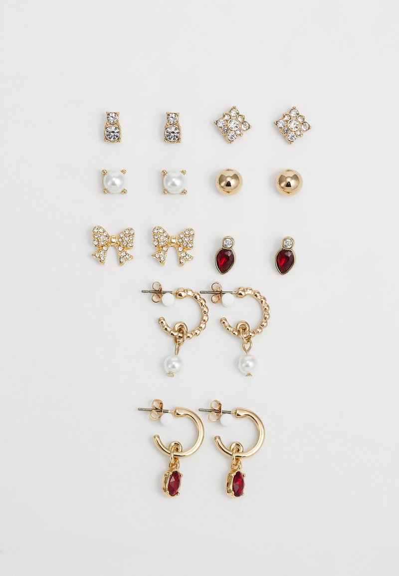 Nueve pares de pendientes de oro y perla, tanto de tachuelas como de aros, con detalles de lazo, cristal y piedras preciosas rojas, dispuestos sobre un fondo blanco.