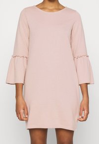 Rosa bomullsklänning med rund halsringning och trekvartsärmar med klockformade detaljer och volanger. Enkel, figurnära siluett och knälång fåll.