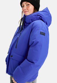 Lila, gepolsterte Jacke mit Kapuze, Frontreißverschluss, zwei seitlichen Taschen und einem schwarzen "ROXY"-Patch am linken Ärmel.