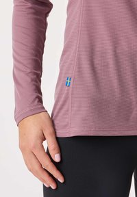 Pitkähihainen, ribbineulottu, violetti urheilupaita, jossa on pieni sinikeltainen Ruotsin lippu sauman kohdalla, yhdistettynä mustiin leggingsseihin.