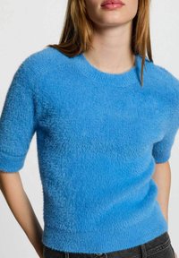 Maglione blu sfocato con maniche corte, scollatura rotonda e orlo a costine. Realizzato in materiale morbido, presenta una superficie testurizzata.