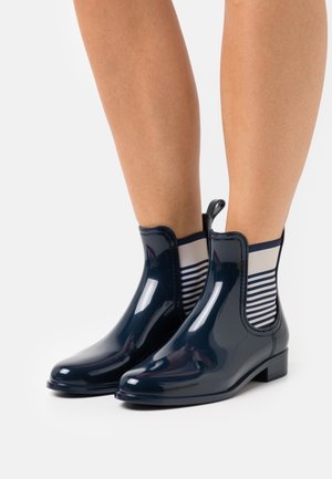 Botas de tobillo de goma azul marino con acabado brillante, paneles laterales elásticos que presentan franjas blancas y azules marinas, y un tacón bajo tipo bloque.