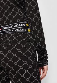 Svart klädsel med ett vitt geometriskt mönster med smiley-ansikten, kompletterat med ett varumärkes-elastisk midjeband i svart med gula accenter.