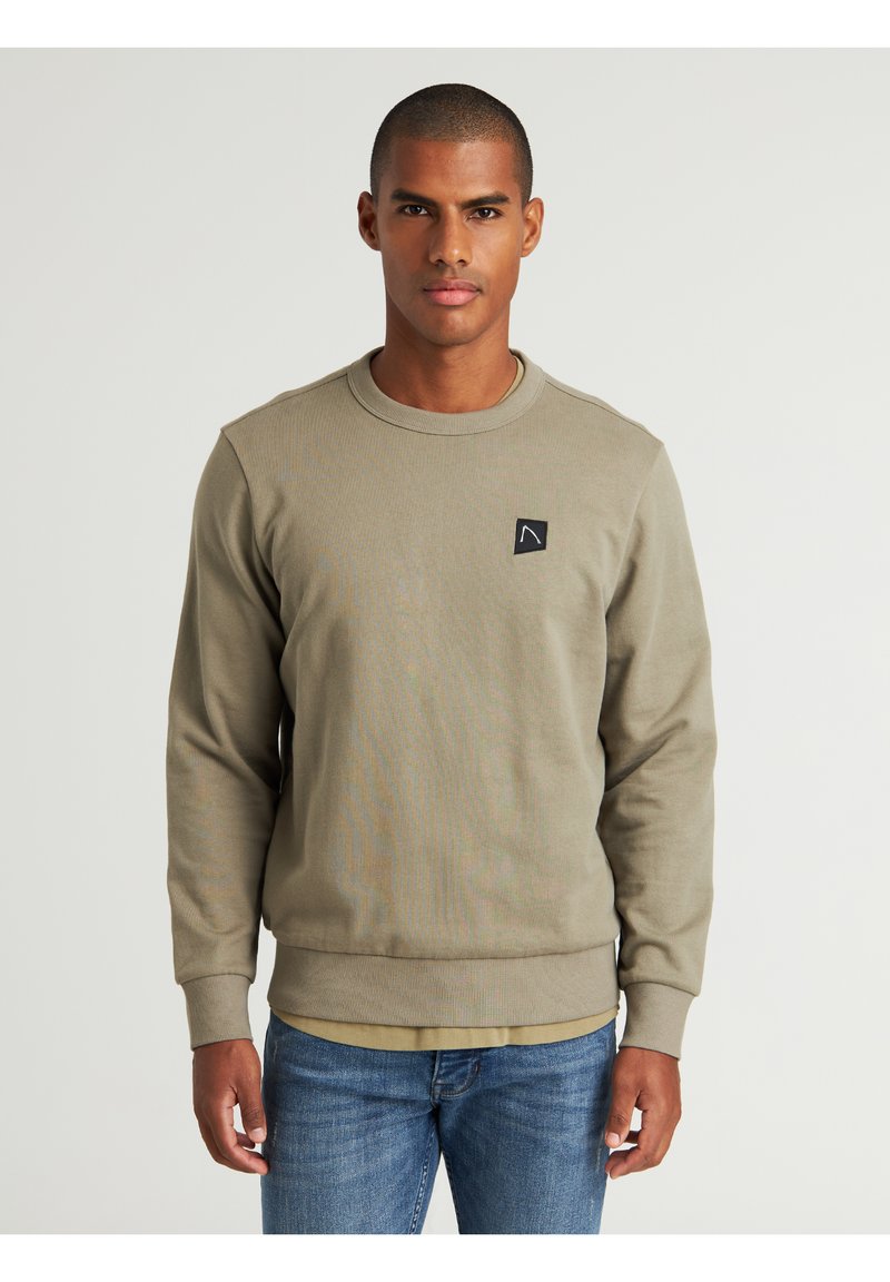 Sudadera de cuello redondo en verde oliva, confeccionada en una mezcla de algodón, con un pequeño parche de logo negro en el lado izquierdo del pecho y puños y dobladillo acanalados.