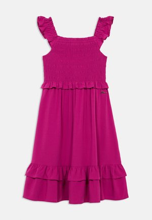 Robe rose vif sans manches avec corsage smocké, bretelles à volants et ourlet à double volant, adaptée à une tenue décontractée ou estivale.