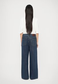 Blå vide jeans laget av denim, med høy midje, store baklommer og en brun lærmerkelapp på linningen.