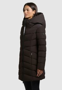 Cappotto imbottito marrone con colletto alto, dotato di chiusura con zip, motivo a rombi obliqui, due tasche laterali e dettagli con marchio.
