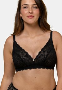 Brassière en dentelle noire avec des bretelles réglables, présentant un décolleté plongeant, des bords festonnés et un petit accent doré au centre.