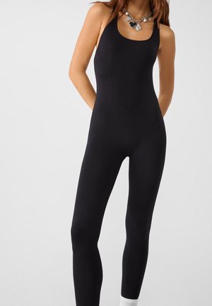 Musta ribbineulottu haalari, jossa on vartalonmyötäinen leikkaus, leveät olkaimet ja pyöreä pääntie. Valkoiset nilkkasukat näkyvissä alareunassa.