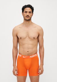 Narančaste boxer kratke hlače iz elastične tkanine z belim pasom z logotipom Nike, ki imajo prilegač dizajn in gladko teksturo.