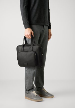Malette en cuir noir avec deux poignées supérieures, poche zippée à l'avant, forme rectangulaire, texture lisse et design minimaliste.
