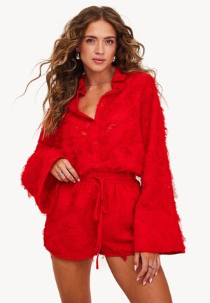 Ensemble rouge texturé composé d'une chemise à boutons ample avec des manches larges et d'un short à cordons assorti. Caractérisé par un tissu doux et effiloché.