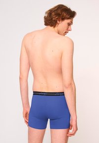 Bóxer azul con una cinturilla elástica negra que lleva el nombre de la marca. La tela parece suave con un diseño ajustado.