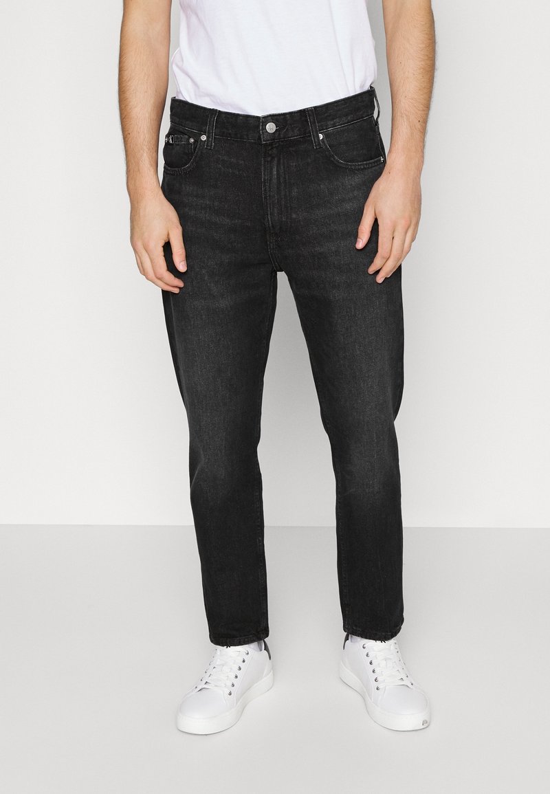 Svarta jeans i denim, rak skärning med blekt utseende, femficksdesign och metallknappsstängning. Bärs med vita sneakers.