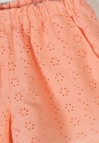 Tissu de couleur pêche avec une ceinture élastique, présentant de petits motifs floraux brodés en ajour tout au long du matériau.