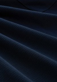 Dunkelblaues, strukturiertes Gewebe mit einem gerippten Muster, das weiche Falten und subtile Schatten aufweist und damit Tiefe im Erscheinungsbild des Materials schafft.